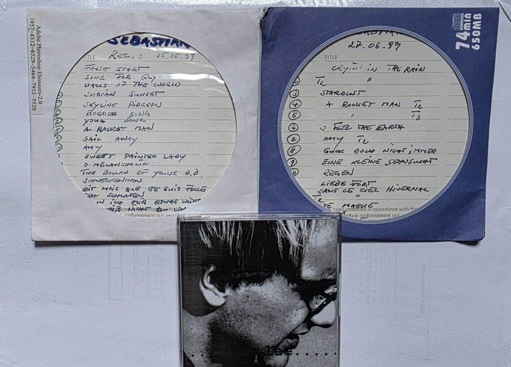 Photograph of two handwritten tape boxes and an early cassette associated with Cian Lee, showing track lists and documenting early demo recordings.