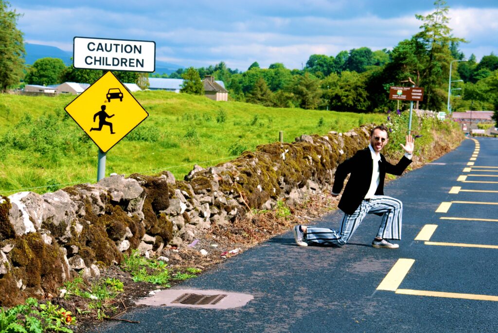 Kian Lee posing playfully on a country road in Ireland beside a caution children road sign during the concept-video shoot.