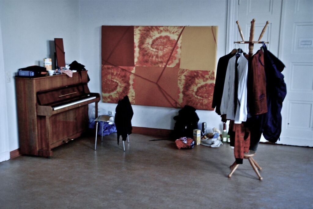 Backstage room with upright piano, clothing rack and artwork on the wall.