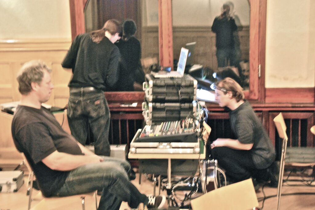 Technical crew working at a recording setup during rehearsal in an interior venue space.